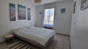 Un dormitorio con una cama, una mesita redonda pequeña, un tapete tejido en el suelo y tres cuadros colgados en la pared.