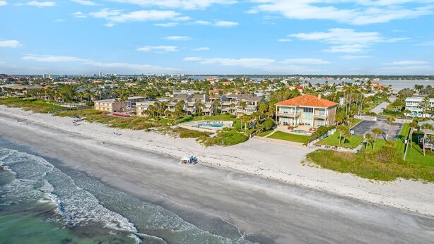 Zona residencial costera con propiedades frente al mar, incluyendo una casa grande con piscina y una playa en primer plano.