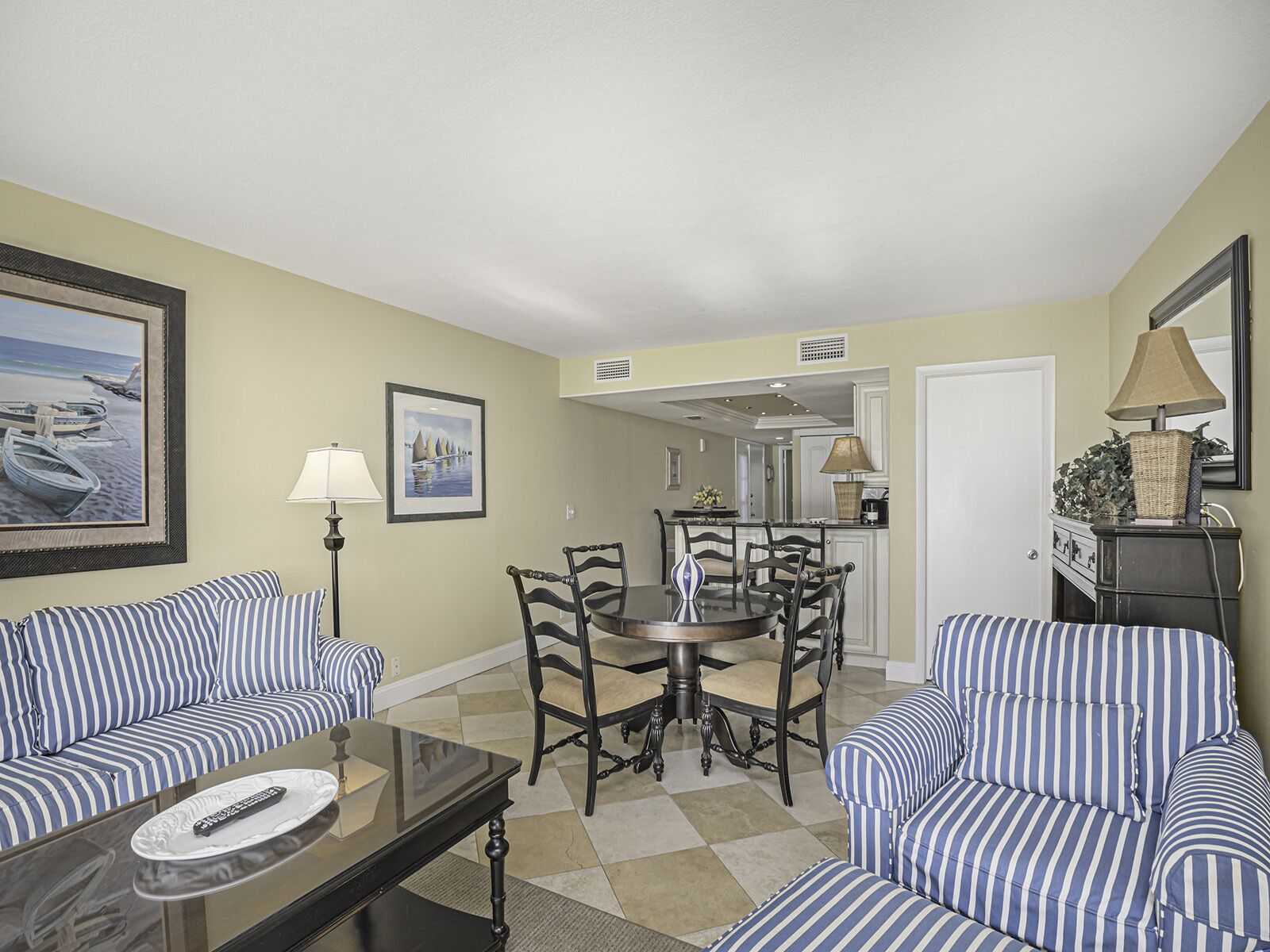 A living room with striped sofas, a glass coffee table, and a dining area with a round table and chairs.