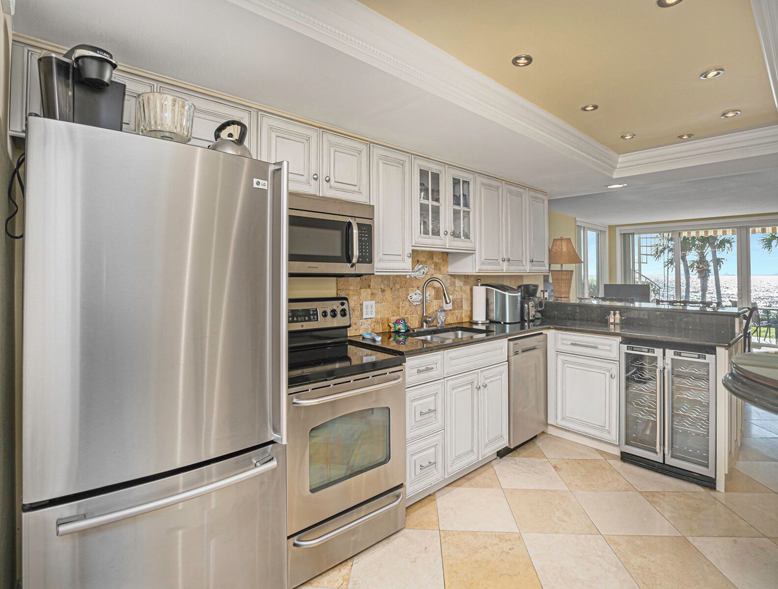 A modern kitchen with stainless steel appliances, white cabinetry, and a large window offering a view of the beach.