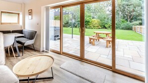 A modern living room with a sliding glass door leading to a patio with a wooden table and chairs. - Tawny Acre Barn - UK38614 (South Walton Highway, Wisbech)