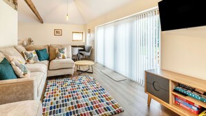 A living room with a sofa, chairs, a coffee table, a TV, and a bookshelf with board games. - Tawny Acre Barn - UK38614 (South Walton Highway, Wisbech)