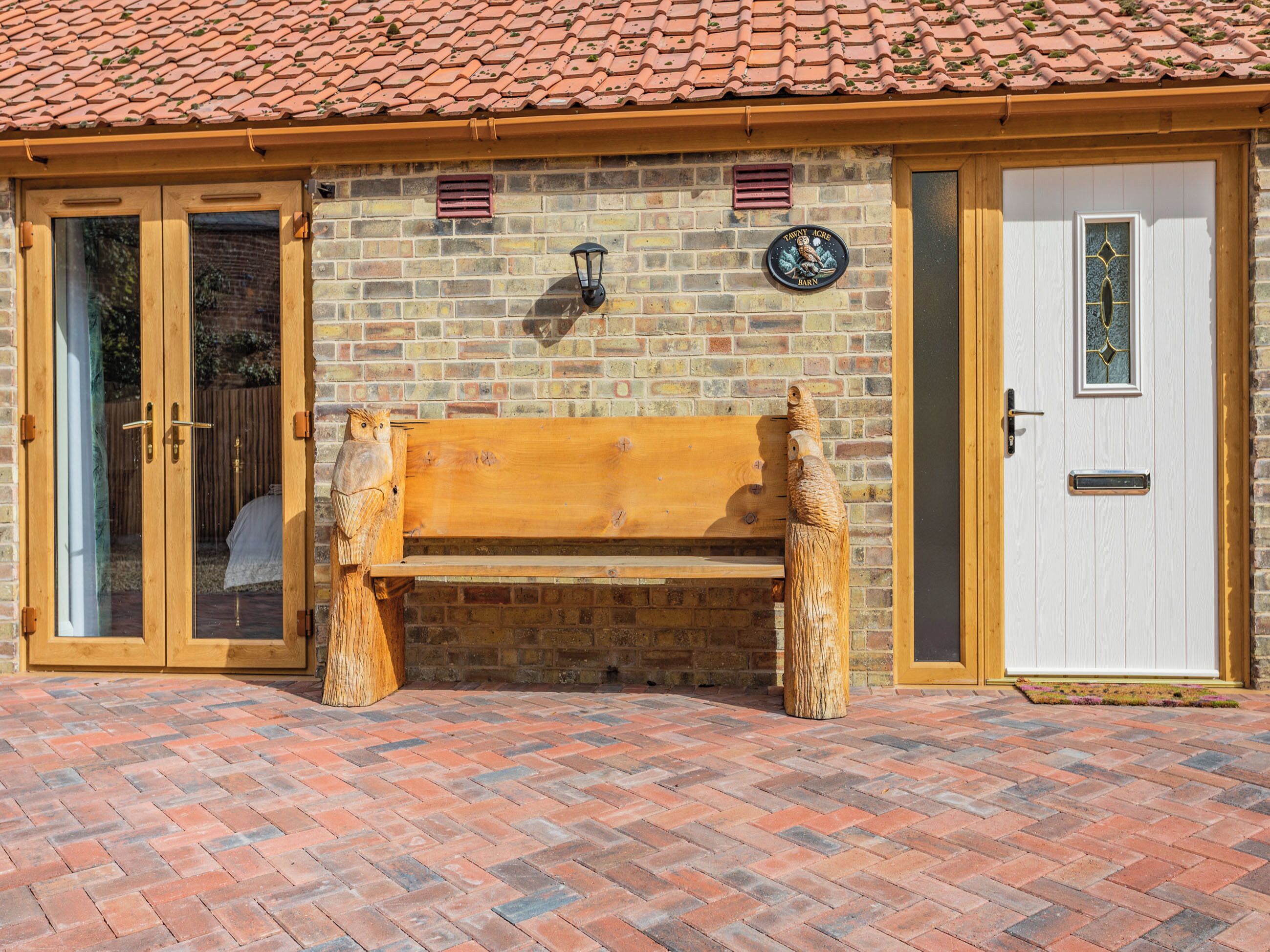 A brick building with a wooden bench, a white door, and a window with a decorative frame.