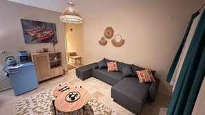 Un salon chaleureux avec un canapé gris, une petite table en bois, une machine à café et un tableau représentant des bateaux accroché au mur.