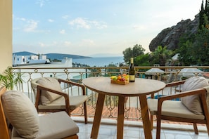 Ein Balkon mit einem runden Holztisch, zwei gepolsterten Stühlen, einer Weinflasche und einer Obstschale.