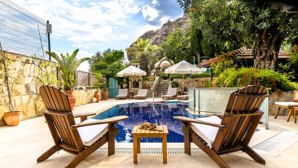 Un espace piscine agrémenté de chaises longues et de parasols, entouré de verdure et délimité par un mur de pierre.