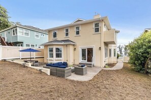 Ein zweistöckiges Haus mit einer Terrasse, die Gartenmöbel und einen blauen Sonnenschirm beinhaltet.