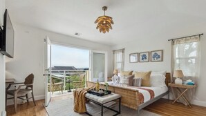 Een ruime slaapkamer met een groot bed, een balkon, een eethoek en een aan de muur bevestigde televisie.