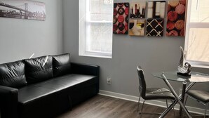 Ein modernes Wohnzimmer mit einer schwarzen Ledersofa, einem Glastisch mit Stühlen und einem Fenster mit Jalousien.