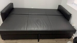 Ein schwarzes Schlafsofa mit Holzboden und weißen Wänden.