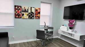 Ein modernes Wohnzimmer mit einem Glastisch, schwarzen Stühlen, einem Wand-Fernseher und Kunstwerken an den Wänden.
