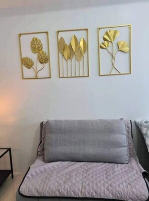 Una cama con cubrecama acolchado y almohada gris, una mesita de noche, y tres obras de arte con hojas enmarcadas en la pared.