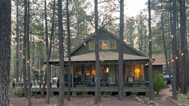 A cabin with a porch, surrounded by trees, and a fire pit in the foreground. - Cozy Pinetop Country Club Home on Golf Course (Pinetop)