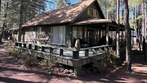 A rustic cabin with a porch, surrounded by tall trees. - Cozy Pinetop Country Club Home on Golf Course (Pinetop)