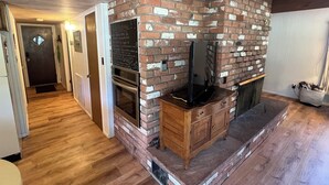A modern kitchen with a brick wall, wooden cabinets, a built-in oven, and a television on a wooden stand. - Cozy Pinetop Country Club Home on Golf Course (Pinetop)