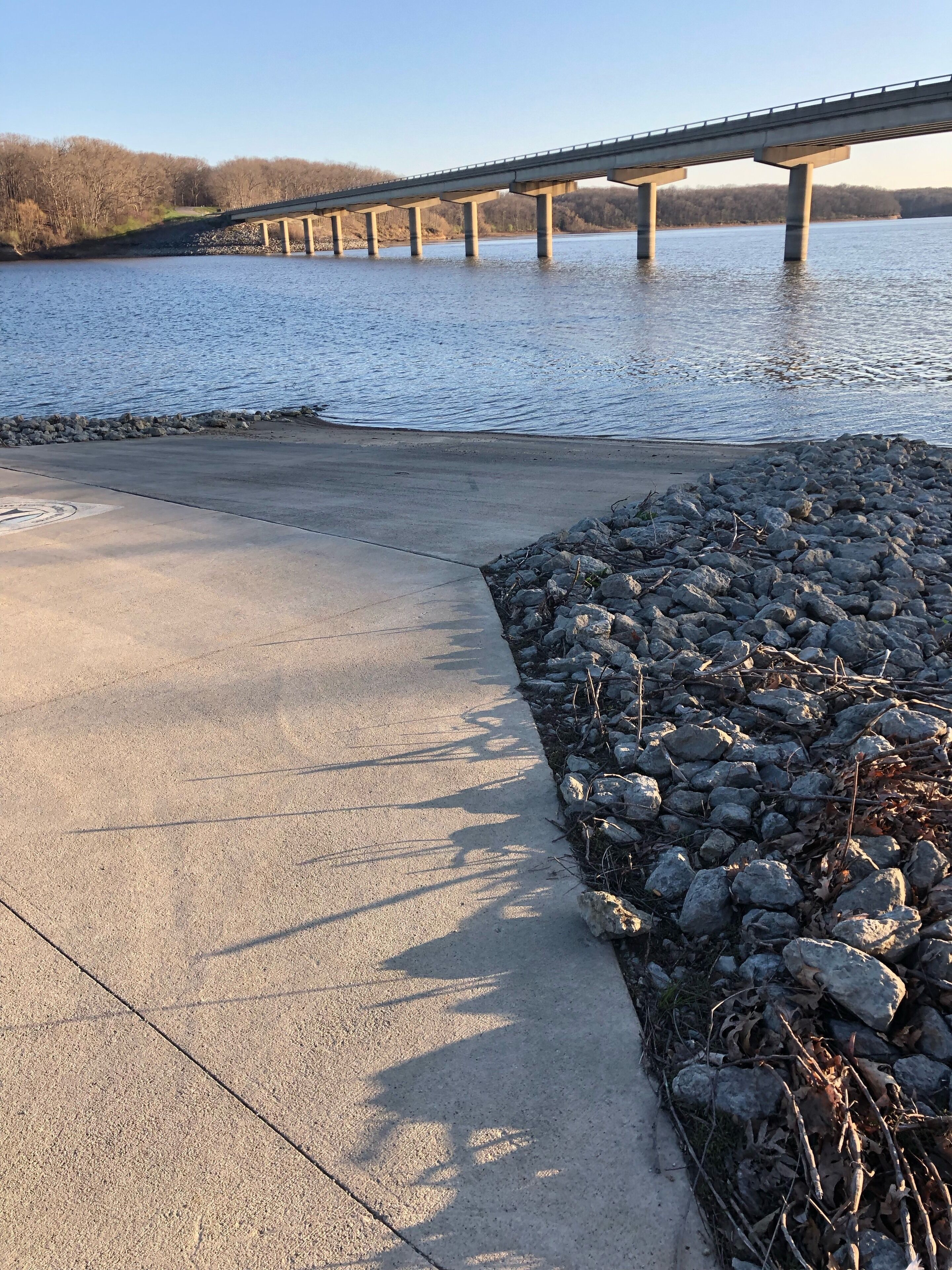 Une promenade en béton au bord d’une rivière, avec un pont en arrière-plan.