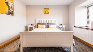 Ein Schlafzimmer mit einem Bett, Nachttischen, einem Heizkörper, einem Fenster mit Jalousien und einer Wand mit einem Gemälde.