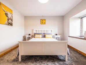 A bedroom with a bed, bedside tables, a radiator, a window with blinds, and a wall with a painting.