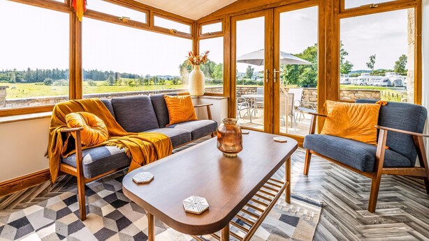 Un solárium con sofá, mesa de centro y sillas, ventanas amplias y vistas al exterior.