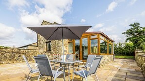 Eine Außenpatio mit Tisch und Stühlen, einem großen Sonnenschirm und einer Steinmauer.