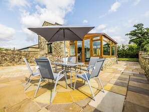 An outdoor patio with a table and chairs, a large umbrella, and a stone wall.