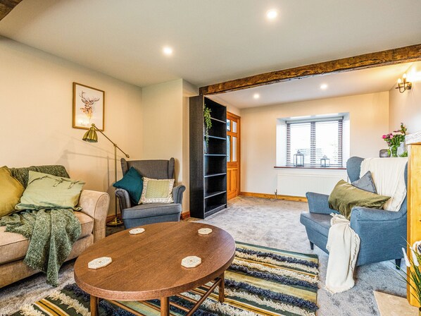 A cozy living room with a sofa, armchairs, a coffee table, and a bookshelf.