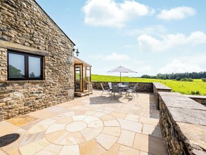 A stone building with a patio area featuring a table and chairs, an umbrella, and a view of a green field.