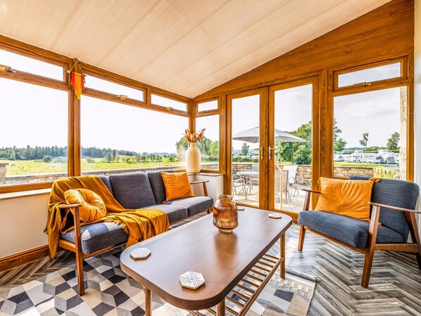 A sunroom with a sofa, coffee table, and chairs, large windows, and a view of the outdoors.