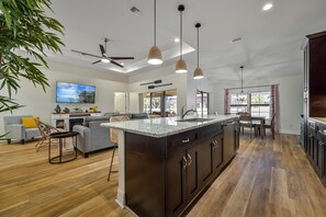 Une cuisine moderne avec des meubles de couleur sombre, un îlot central, des luminaires suspendus et un coin repas comprenant une table et des chaises.