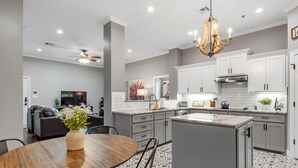 A modern kitchen with white cabinets, a central island, and a dining area with a wooden table and chairs. - Walk to Magnolia • 2 Minutes to Baylor • Huge Private Balcony • King Beds (Waco)