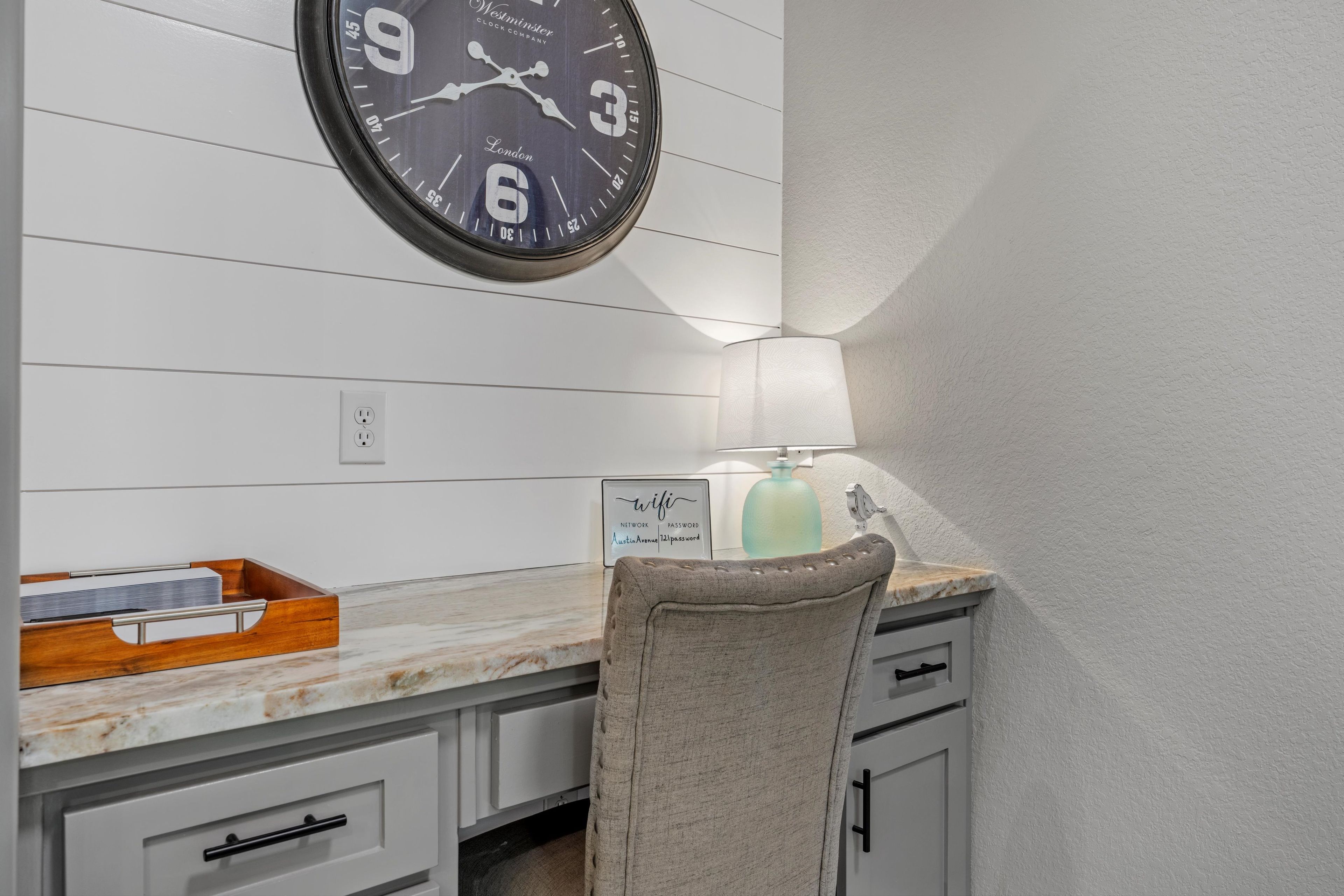 A kitchen with a clock, a wooden tray, a lamp, and a chair.