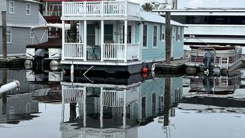 Una casa flotante con balcón pequeño, zona cubierta y letrero con su nombre.