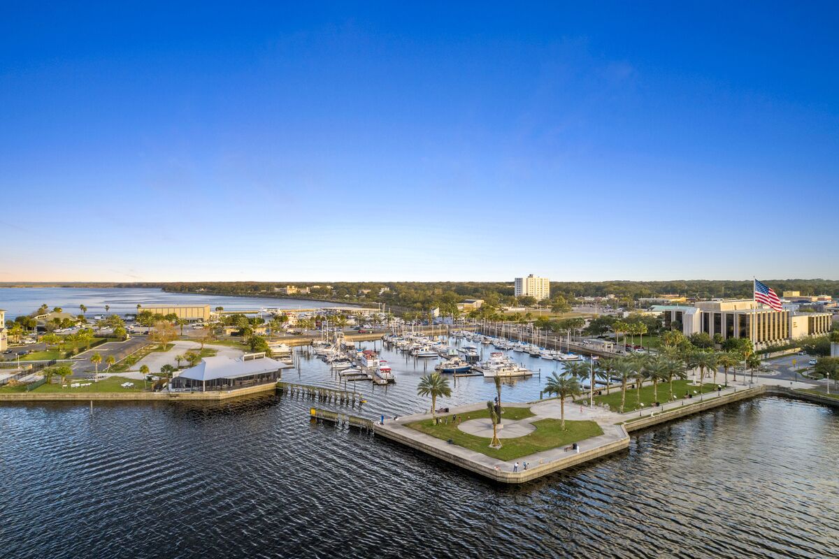 A marina with boats docked, a flagpole with an American flag, and a building with a modern design.