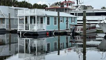 Una casa flotante amarrada en un puerto deportivo, con una pequeña terraza y un porche cubierto.