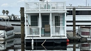 A houseboat docked at a marina with a white exterior, a balcony, and a small deck area.