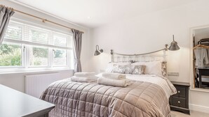 A bedroom with a bed, bedside lamps, a dresser, and a window with curtains.
