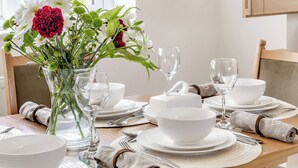 A dining table set with white plates, bowls, and cutlery, a vase with flowers, and a clear glass.