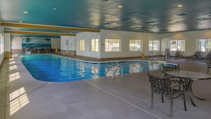 An indoor swimming pool with a mural of a beach scene, a poolside table with chairs, and multiple windows allowing natural light.