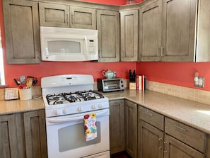 A kitchen with wooden cabinets, a microwave, a gas stove, a toaster, and various kitchen utensils.