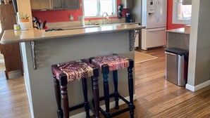 A kitchen with wooden cabinets, a granite countertop, and two bar stools with colorful cushions.