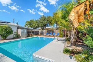 Une piscine dotée de chaises longues et d’un espace abrité, entourée de plantes tropicales et d’une clôture en bois.