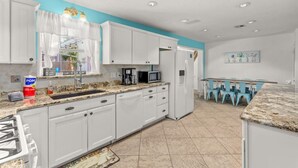 A modern kitchen with white cabinets, a granite countertop, and a dining area with blue chairs.