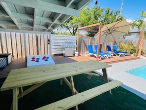Un espace aménagé au bord de la piscine, avec une table en bois, des chaises longues bleues et un coin salon abrité.