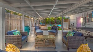 An outdoor patio area with wicker furniture, a wooden coffee table, and a pool in the background.