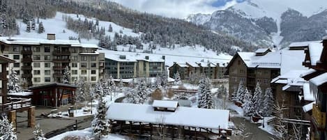 Een met sneeuw bedekt resort met meerdere gebouwen, een rivier en bergen op de achtergrond.