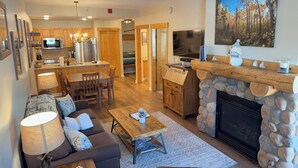 A modern living room with a fireplace, a dining area, and a kitchen with wooden cabinets and a large TV. - Tucker Mountain Lodge @ Copper Mountain (Copper Moutain)