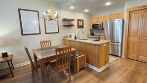 A kitchen with wooden cabinets, a stainless steel refrigerator, a microwave, and a dining area with a table and chairs. - Tucker Mountain Lodge @ Copper Mountain (Copper Moutain)