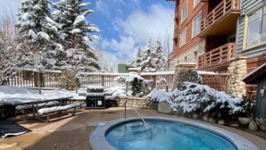 A pool area with a hot tub, surrounded by snow-covered trees and a stone wall. - Tucker Mountain Lodge @ Copper Mountain (Copper Moutain)