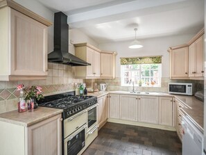 A kitchen with wooden cabinets, a black stove, and a window with a view of greenery. - 6 bedroom accommodation in Dorrington, near Church Stretton (Dorrington, near Church Stretton)