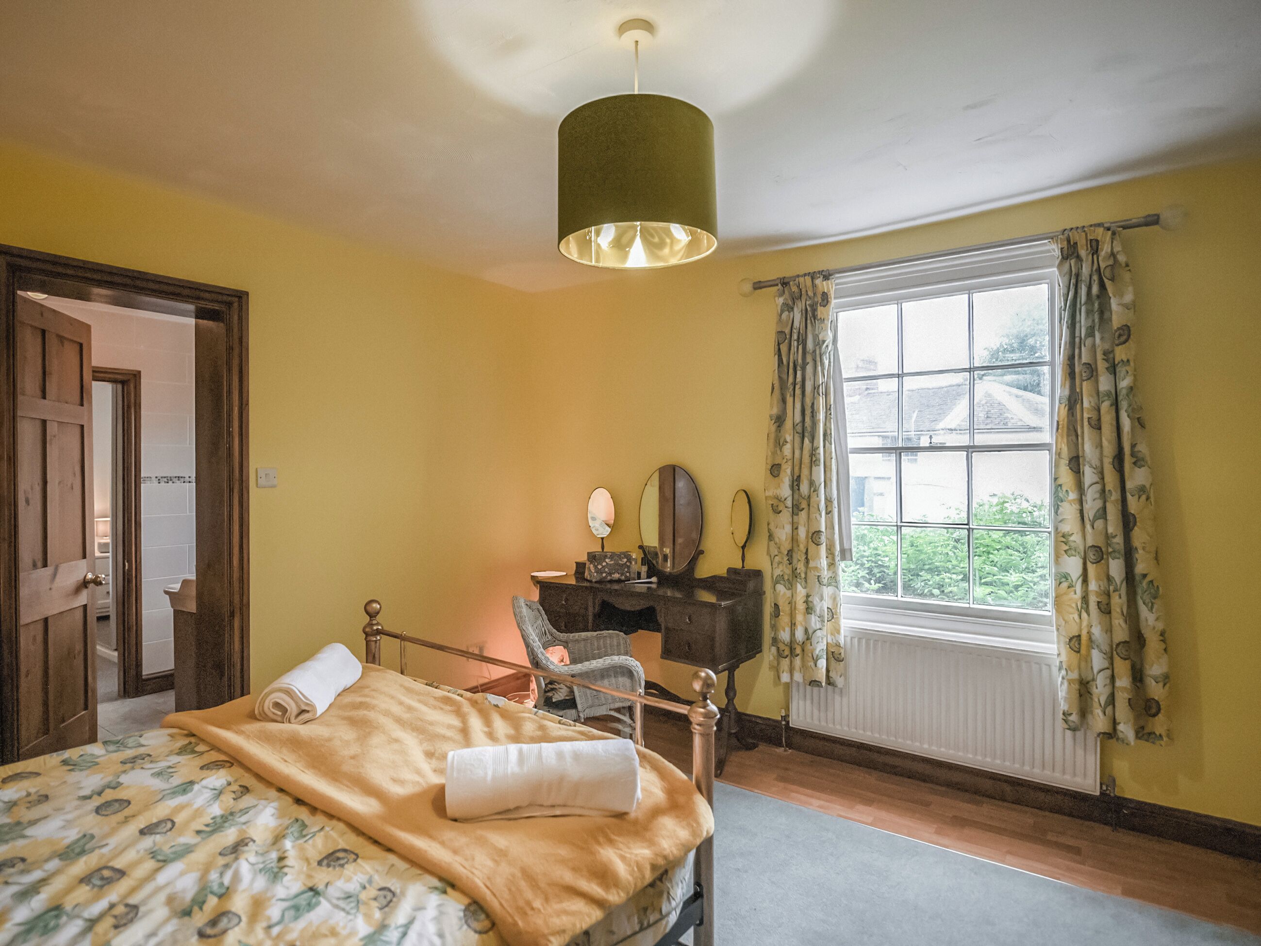 A bedroom with a bed, a wooden dresser, a mirror, a window with curtains, and a door.